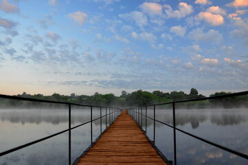 Long bridge crossing the river or lake. Wooden old bridge perspective in early morning with blue...