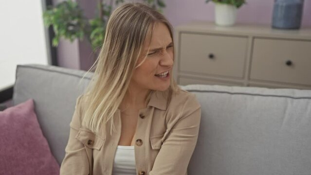 Young blonde woman sitting on sofa angry and mad screaming frustrated and furious, shouting with anger. rage and aggressive concept. at home