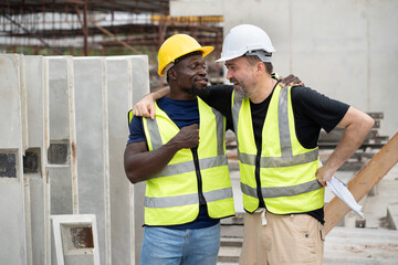 Portrait happy caucasian engineer man shoulder hug with happy African engineer man at precast cement outdoor factory	