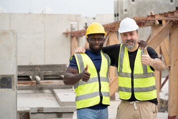 Portrait happy caucasian engineer man shoulder hug with happy African engineer man at precast cement outdoor factory	