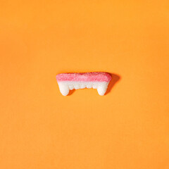 Gummy vampire teeth, sweet and sour Halloween candy isolated on orange background