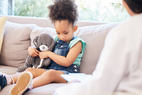 Child, sad and therapy in clinic for mental health, depression and conversation in doctors office. Young, girl and teddy bear for support, psychology and wellness for trauma on couch with therapist