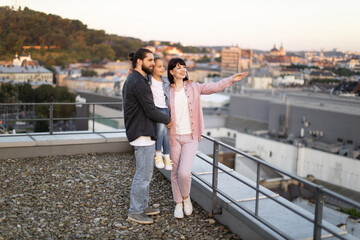 Young family enjoying panoramic view from rooftop, happy moment together at sunset, urban cityscape background.