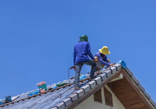 Repairmans repairing leaking ridges tile roofing and replace cracked broken tile roofing on  blue  sky  background.