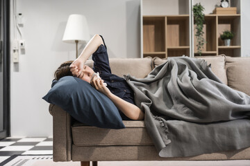A young female Asian is resting on a sofa, suffering from the flu. She shows symptoms like fever,...