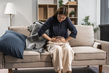A young female Asian is resting on a sofa, experiencing menstrual cramps. She has pelvic pain,...