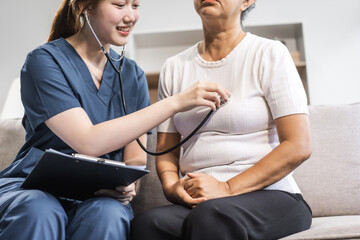 A young female nurse of Asian descent provides care to an elderly patient, a woman, sitting on a...