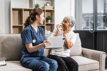 A young female nurse of Asian descent provides care to an elderly patient, a woman, sitting on a...