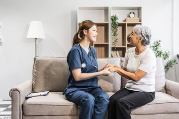 A young female nurse of Asian descent provides care to an elderly patient, a woman, sitting on a...
