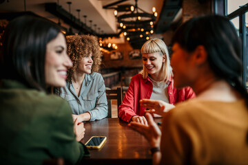 Four female friends having a great time in cafe, sitting, and about to order drinks and food