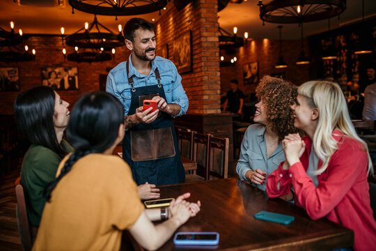 A diverse group of smiling friends giving a server their order while sitting at a table together indoors