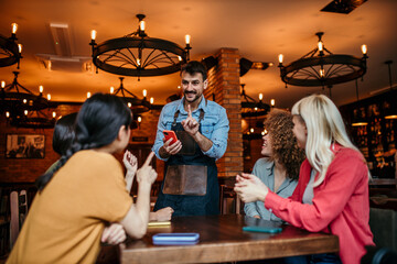 A group of young adults ordering coffee and a mid-adult waiter patiently listening and writing it down on a smartphone