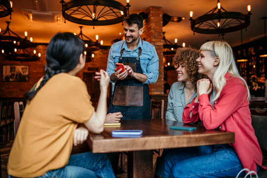 A diverse group of smiling friends giving a server their order while sitting at a table together indoors