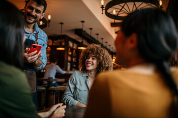 A group of young adults ordering coffee and a mid-adult waiter patiently listening and writing it down on a smartphone