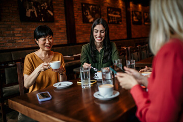 Four Young Diverse Female Friends Meeting Sit At Table In Coffee Shop And Talk
