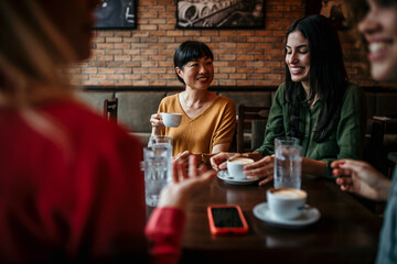 Smiling diverse female friends sit in a cafe laughing and talking over a coffee