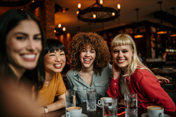 Group of smiling female friends sitting in the bar and taking a selfie for a social media
