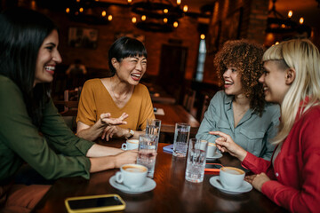 Group of smiling diverse females sitting in the restaurant, having a coffee and chatting