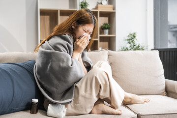 A young female Asian is sitting on a sofa, wrapped in a shawl. She is experiencing cold symptoms...
