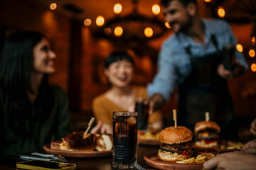 Two female friends are having fun while a waiter is serving them food and drinks in a pub