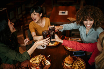 Multi-ethnic group of friends sitting in restaurant and cheering with soft drinks