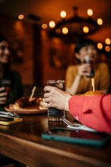 Unrecognizable woman holding a glass of soft drink while having a lunch with her friends