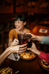 Multi-ethnic group of friends sitting in restaurant and cheering with soft drinks