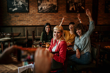 Group of a smiling female friends having a lunch together and being photograph by the waiter