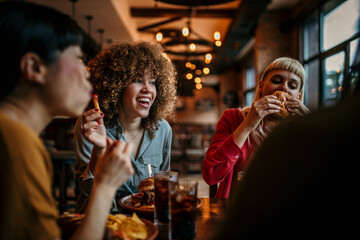 Young happy women eating burgers and talking in a pub