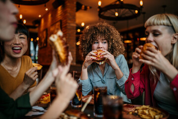 Fototapeta premium Hungry woman eating a burger while gathering with friends in a pub
