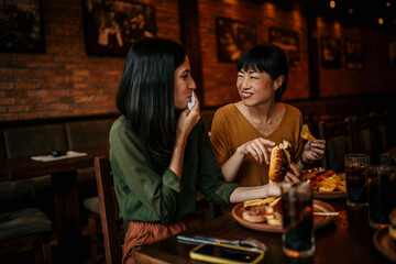 Hungry woman eating food while gathering with her friend in a pub