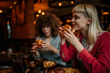 Two multiracial happy friends eating burgers and enjoying a time together in a pub