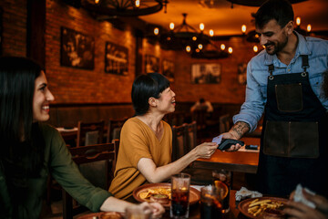 Shot of two women talking witha a waiter while making a card payment using a NFC machine