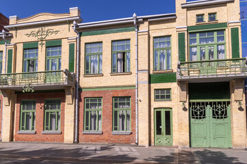 The facade of an ancient building with green metal gates and balconies. The brick facade of the...