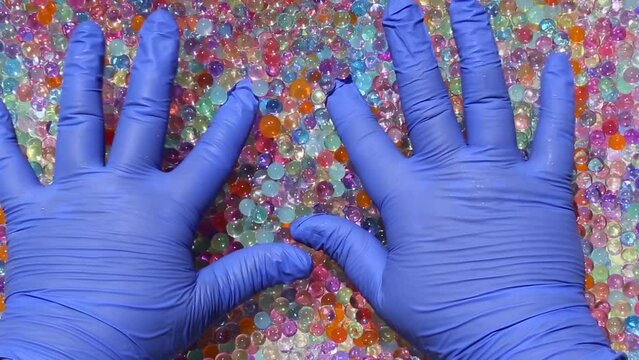 Hands in blue gloves are playing with multicolored orbis. Fingers dip and wiggle, pressing a multitude of colored orbis. Playful, uplifting. Asmr. Part7.14