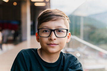 Blond-haired Latino boy with glasses, happy on a high floor of a building. Portrait, childhood,...