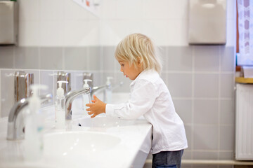 Little preschool child, blond boy, washing hands in bathroom in kindergarden