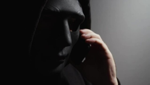 Money swindler, a man in a mask talking on the phone, committing online theft of digital currency.