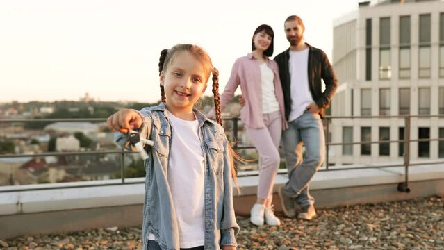 Smiling little girl holding key with family standing in background on rooftop. Concept of new home, family happiness, and real estate.