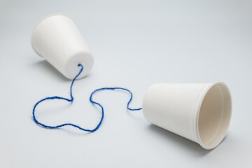 White paper cups with blue string on white background, old style cup phone for communication, and...