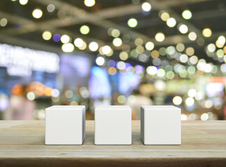 Three white block cubes on wooden table over blur light and shadow of shopping mall