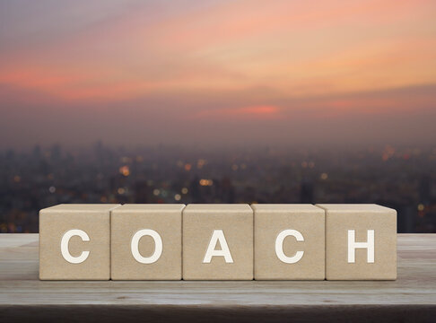 Coach letter on wood block cubes on wooden table over blur of cityscape on warm light sundown, Business, education and learning concept