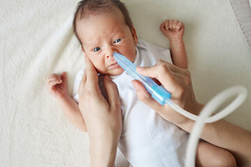 Tender anonymous mother treating her baby's flu with suction pump using aspirator to clean her...