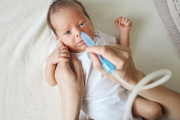 Loving mom is cleaning her baby's nose with a nasal blower using a nasal cleaner on her sick child...