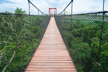 Obraz premium The sky bridge walkway above is a wooden staircase with sunlight. People walk or have the wind secretly swaying, it's exciting to see view or survey route of forest at Walailak University ,Thailand.