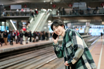 asian man waiting for train while talking on a smart phone. copy space for text.