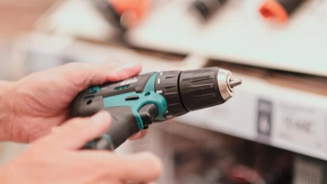 man in a hardware store chooses a new screwdriver or drill next to a showcase of power tools for repairs in the house. hands closeup with tool. 4K