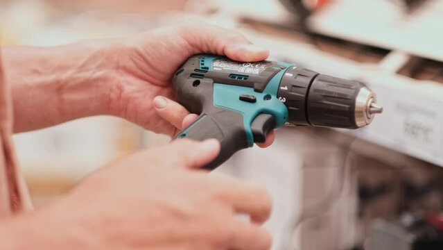 man in a hardware store chooses a new screwdriver or drill next to a showcase of power tools for repairs in the house. hands closeup with tool. 4K