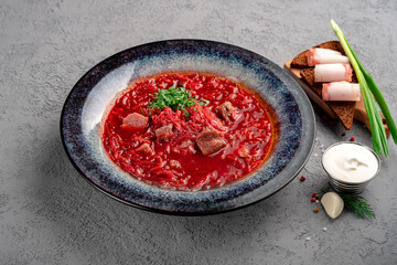 Tomato Soup with beef cabbage and vegetables in a blue plate on a gray background. Russian soup Borscht with tomato paste and sour cream