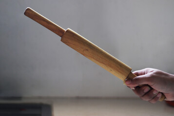 Woman’s hand holding belan or wooden roller or Brown Wooden Rolling Pin
